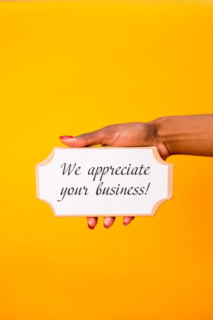A hand holding a sign with'We appreciate your business!' against a yellow background.